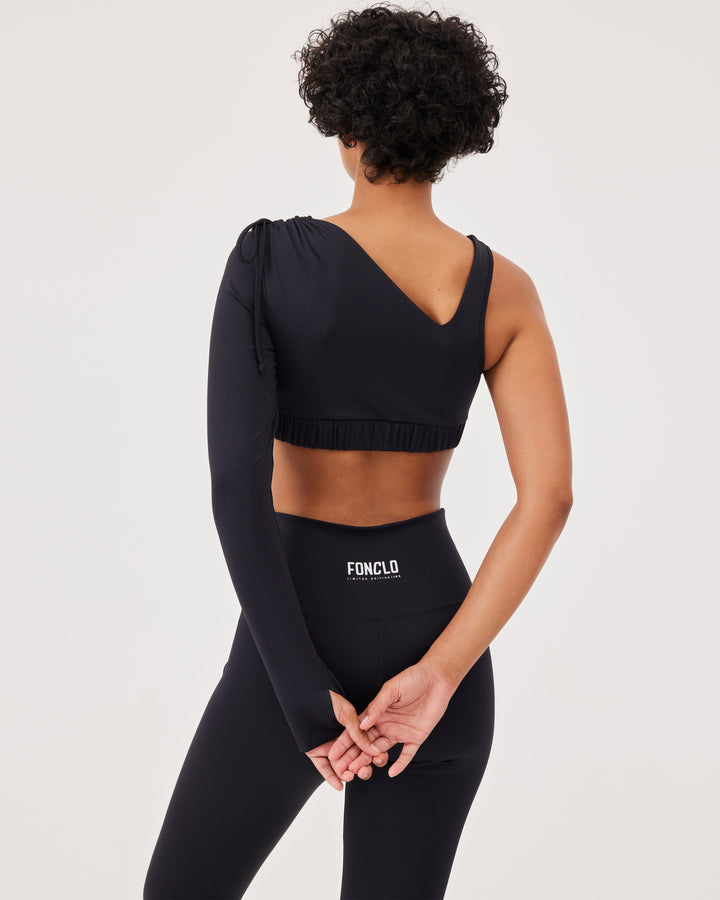 Black asymmetrical cropped top, asymmetrical sleeves, lacing on the shoulder, elastic waistband, slim fit, one long sleeve, thumb hole, sports bra. 